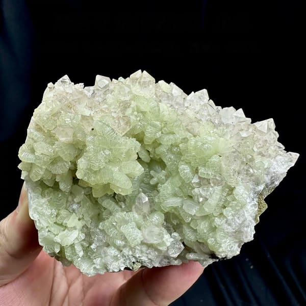 Mound of pale green fan-shaped prehnite from Morocco, held in hand