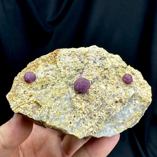 Three raspberry-pink fluorite balls on pale sandstone from Henan, China, held in hand