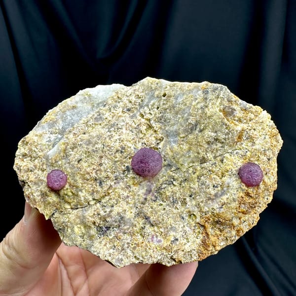 Three raspberry-pink fluorite balls on pale sandstone from Henan, China, close-up of the crystal faces