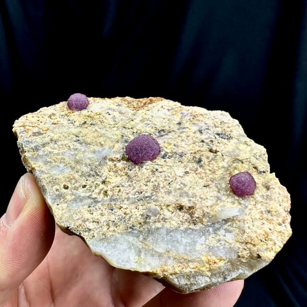 Three raspberry-pink fluorite balls on pale sandstone from Henan, China, reverse side