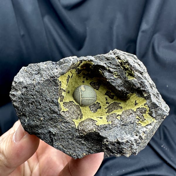 Matcha-green calcite ball inside yellow-lined rock pocket from Fujian, China, close-up of the crystal faces
