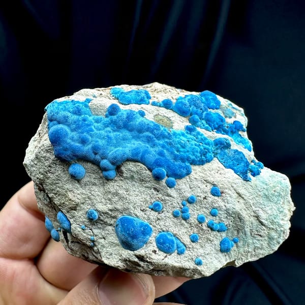 Bright blue chrysocolla balls on grey rock from DR Congo, held in hand