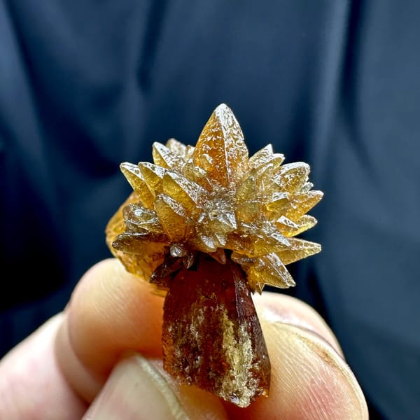 Single amber calcite flower of radiating crystals from Guizhou, China, held in hand