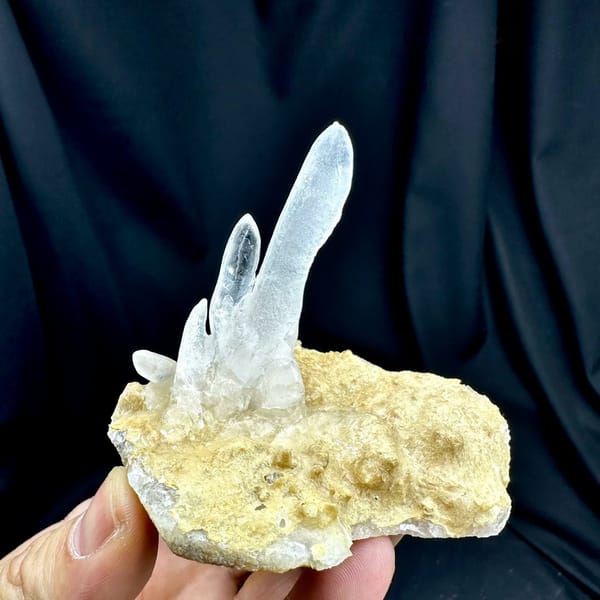 Transparent icicle calcite stalactites on tan base from Yunnan, China, held in hand