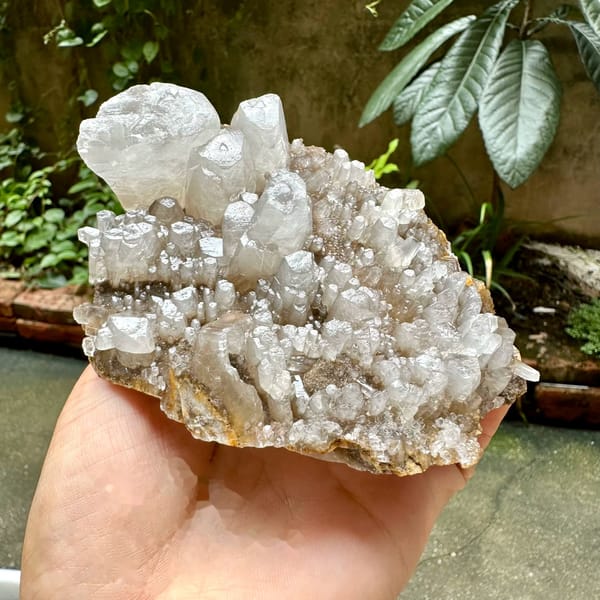 Pale plate of stubby prismatic calcite crystals from Guangxi, China, held in hand