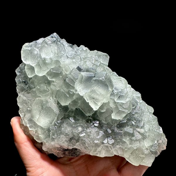 Mound of pale green stepped fluorite cubes from Fujian, China, held in hand