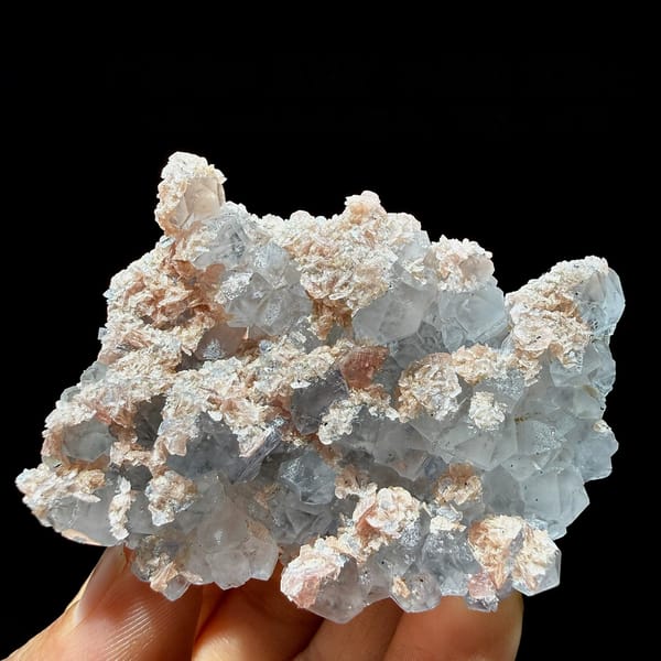 Pale blue fluorite cubes with pink rhodochrosite crusts from Guangxi, China, held in hand