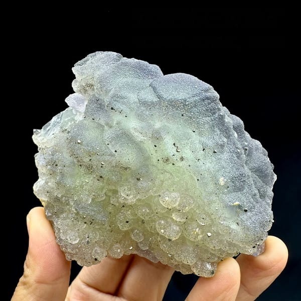 Frosted purple-green fluorite balls dusted with pyrite from Jiangxi, China, held in hand
