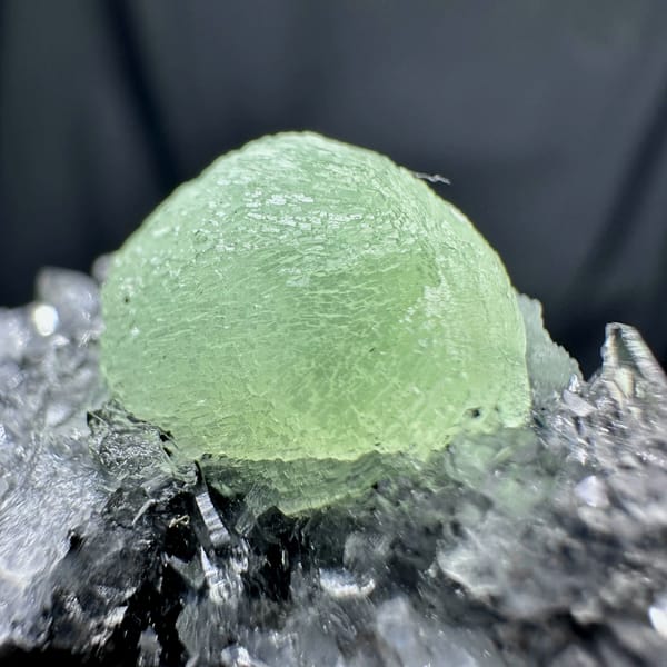 Pale green prehnite ball on dark quartz druse from Sichuan, China, close-up of the crystal faces