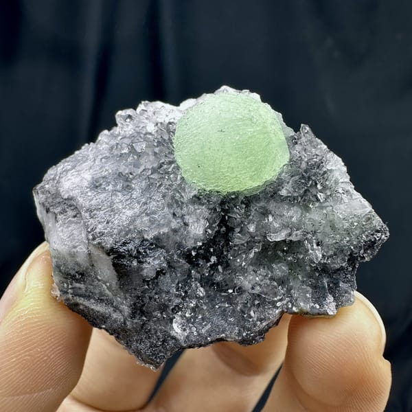 Pale green prehnite ball on dark quartz druse from Sichuan, China, detail of the matrix contact
