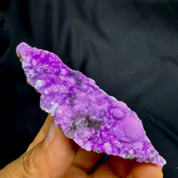 Slender wedge of vivid magenta aragonite from Yunnan, China, held in hand