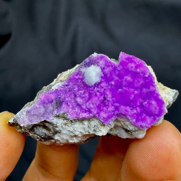 Vivid magenta aragonite with white aragonite tuft from Yunnan, China, held in hand