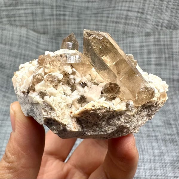 Smoky quartz points on cream feldspar from Yunxiao, Fujian, China, held in hand
