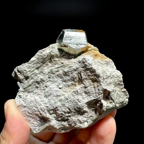 Single pyritohedral pyrite crystal on grey rock slab from Guangxi, China, held in hand