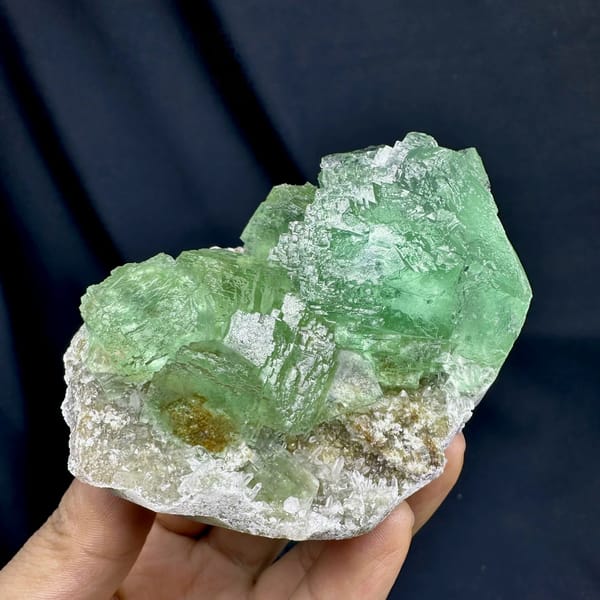 Glassy green fluorite cubes on white quartz druse from Fujian, China, held in hand