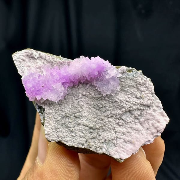 Pink aragonite band across pale grey matrix from Yunnan, China, held in hand