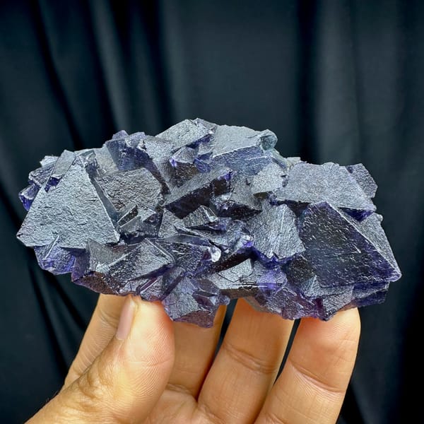 Purple and green octahedral fluorite glowing when, from Zhejiang, China, front view in daylight, held in hand