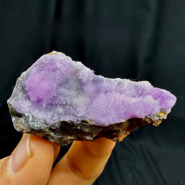 Sparkling magenta aragonite on dark wedge from Yunnan, China, held in hand