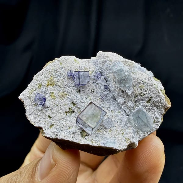 Purple-framed clear fluorite cubes on grey quartz from Inner Mongolia, China, held in hand