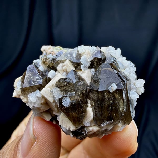 Dark smoky quartz crystals with white feldspar and mica from Yunxiao, Fujian, China, held in hand