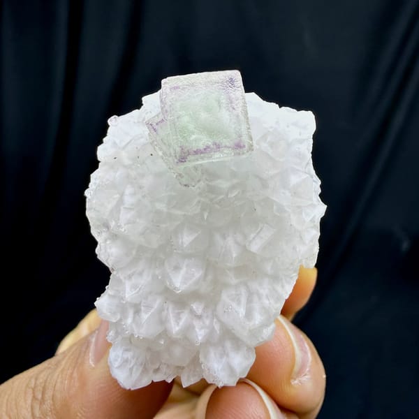 Purple-framed green fluorite cube on white quartz stalk from Zhejiang, China, held in hand