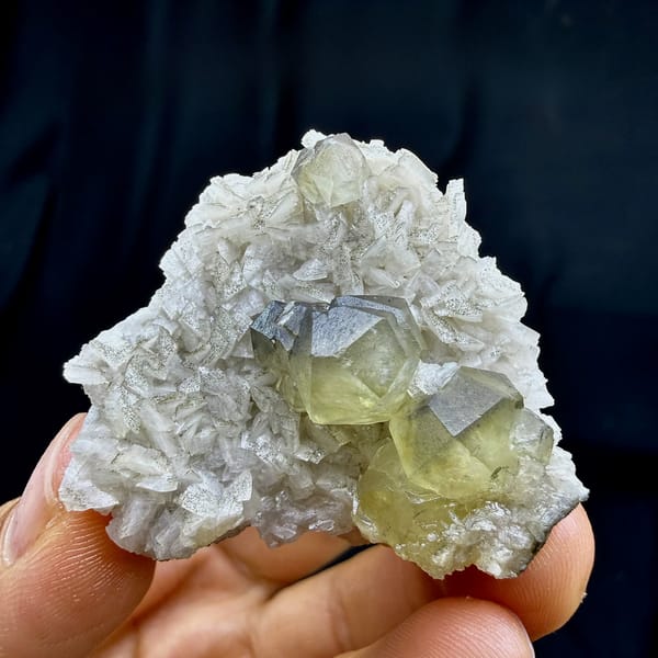 Pale yellow calcite crystal on cream dolomite rhombs from Guizhou, China, held in hand