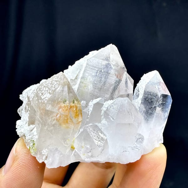 Clear garden-quartz cluster with orange inclusion from Sichuan, China, held in hand