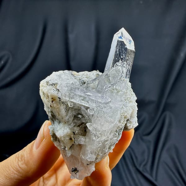 Tall clear quartz prism rising from cream feldspar from Yunxiao, Fujian, China, held in hand