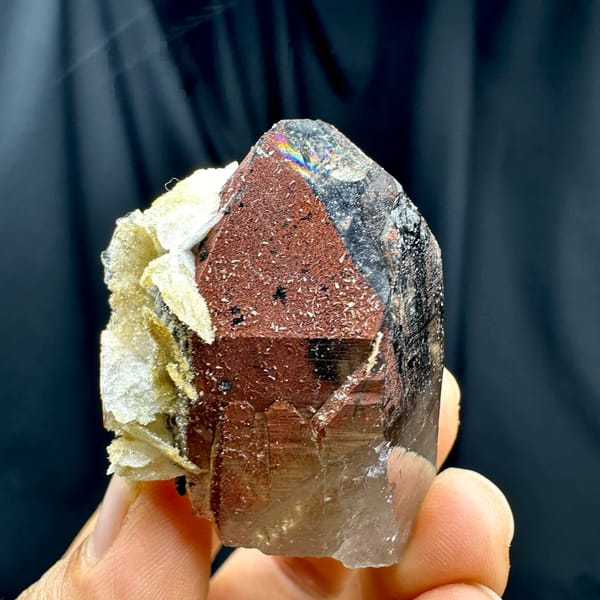 Red-skinned smoky quartz crystal with cream calcite from Yunxiao, Fujian, China, held in hand