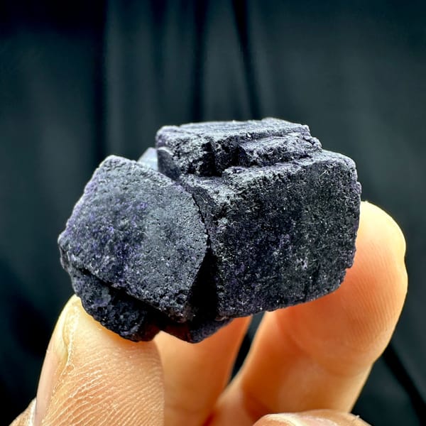 Two black-purple fluorite cubes with matte skin from Inner Mongolia, China, held in hand