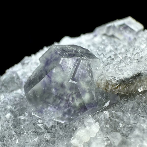 Transparent purple-zoned fluorite dodecahedron on white quartz from Fujian, China, close-up of the crystal faces