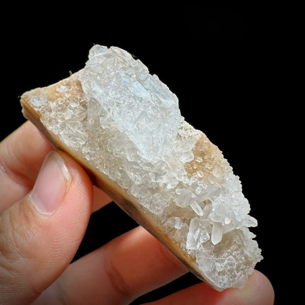 Pale baryte crystal with quartz druse on tan base from Jinkouhe, Sichuan, China, held in hand