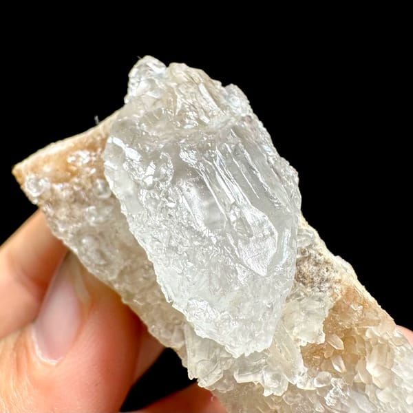 Pale baryte crystal with quartz druse on tan base from Jinkouhe, Sichuan, China, close-up of the crystal faces