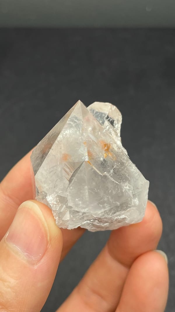 Large clear quartz crystal with rust-orange inclusions from Meigu, Sichuan, China, close-up of the crystal faces