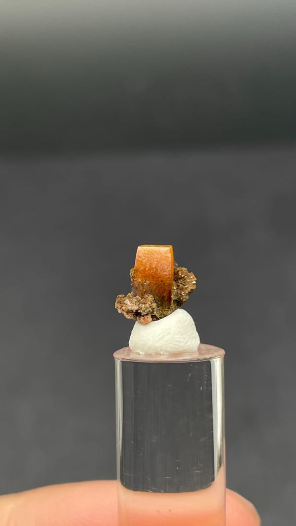 Small orange tabular wulfenite crystal on matrix from Mexico, shown on a stand, close-up of the crystal faces