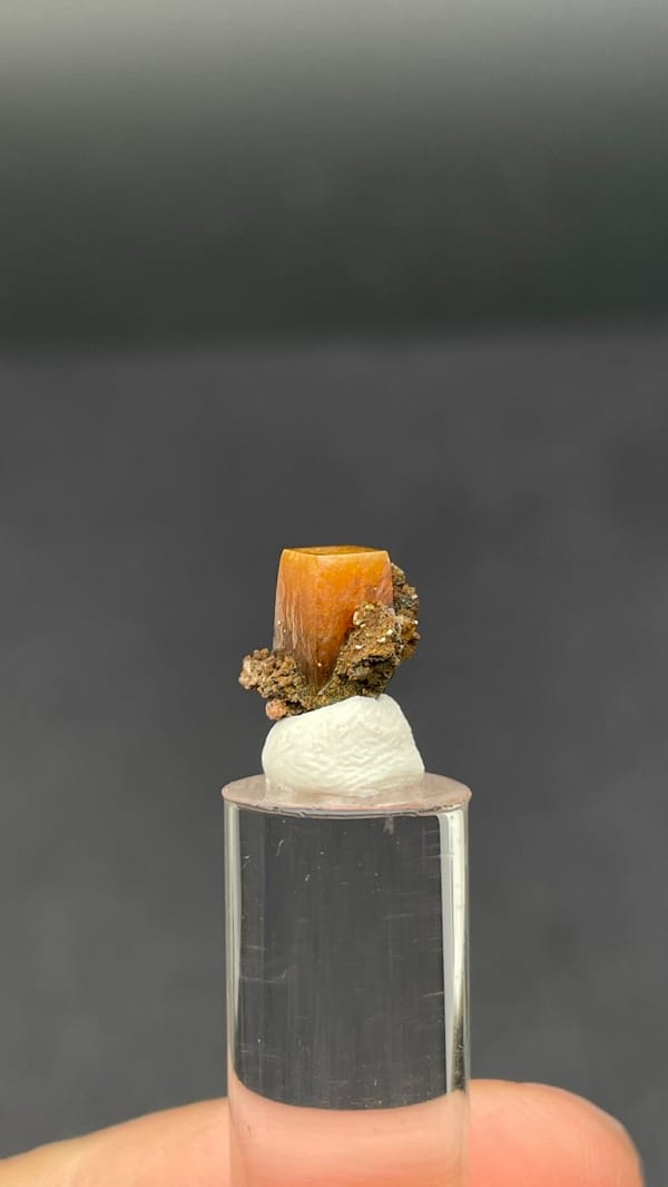 Small orange tabular wulfenite crystal on matrix from Mexico, shown on a stand, reverse side