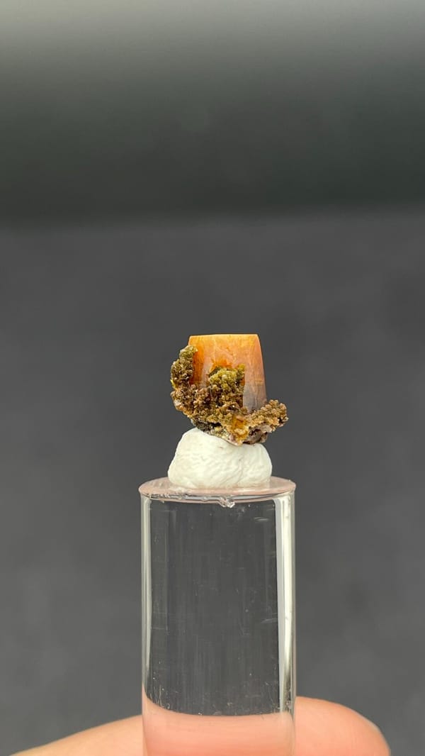 Small orange tabular wulfenite crystal on matrix from Mexico, shown on a stand, detail of the matrix contact
