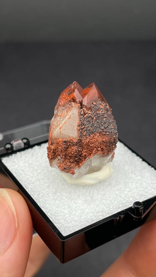 Pink-red quartz point with dark hematite crust from Shanxi, China, in a box, second angle