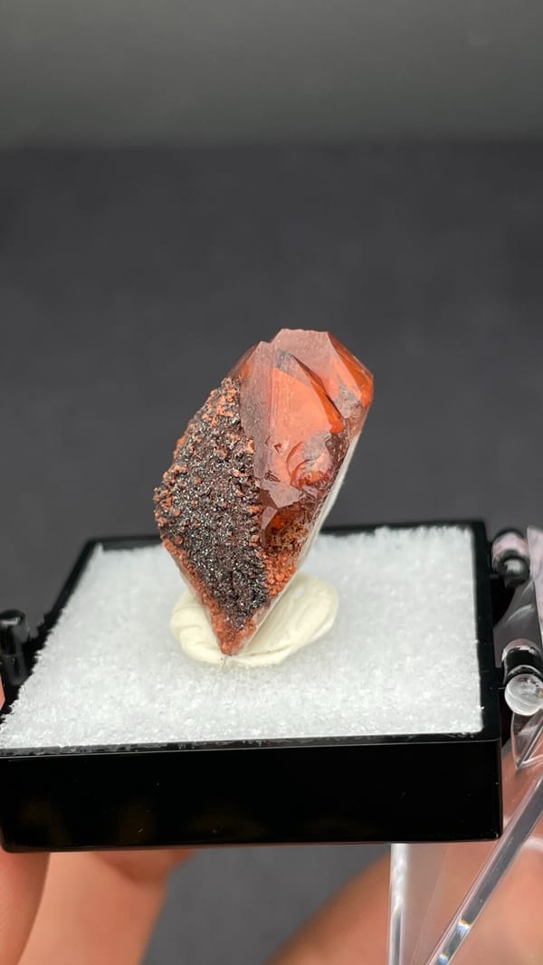 Pink-red quartz point with dark hematite crust from Shanxi, China, in a box, close-up of the crystal faces