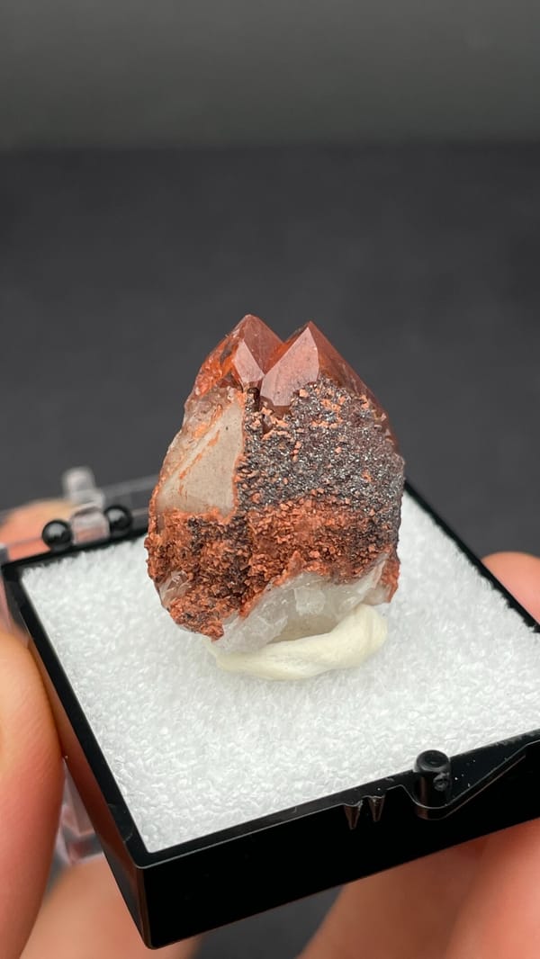 Pink-red quartz point with dark hematite crust from Shanxi, China, in a box, top view