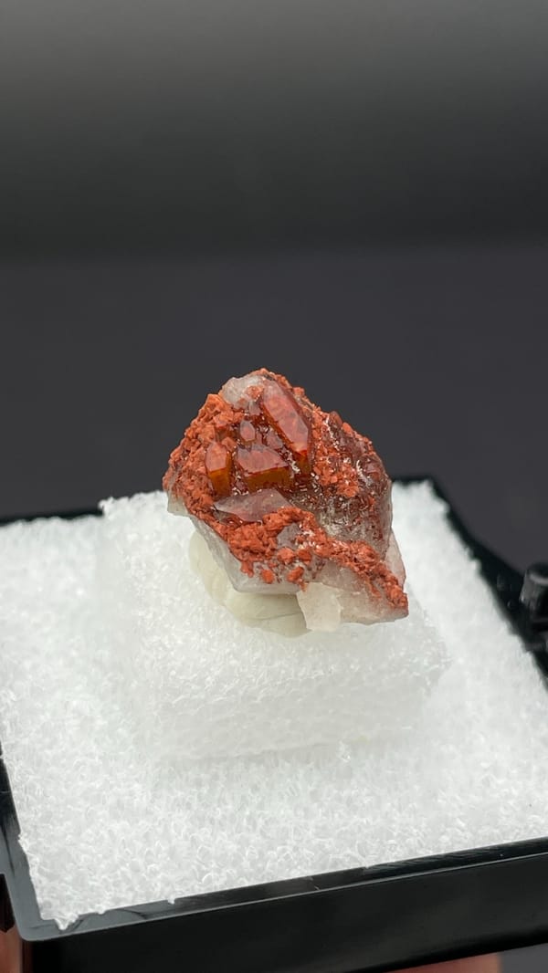 Small deep red hematoid quartz crystal group from Shanxi, China, in a display box, detail of the matrix contact