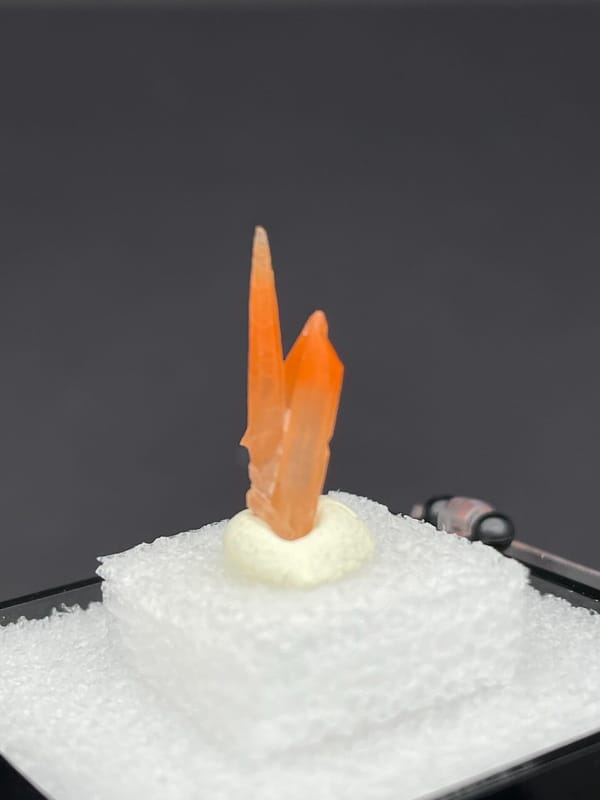 Slim orange-red hematoid quartz point from Guangdong, China, in a display box, close-up of the crystal faces