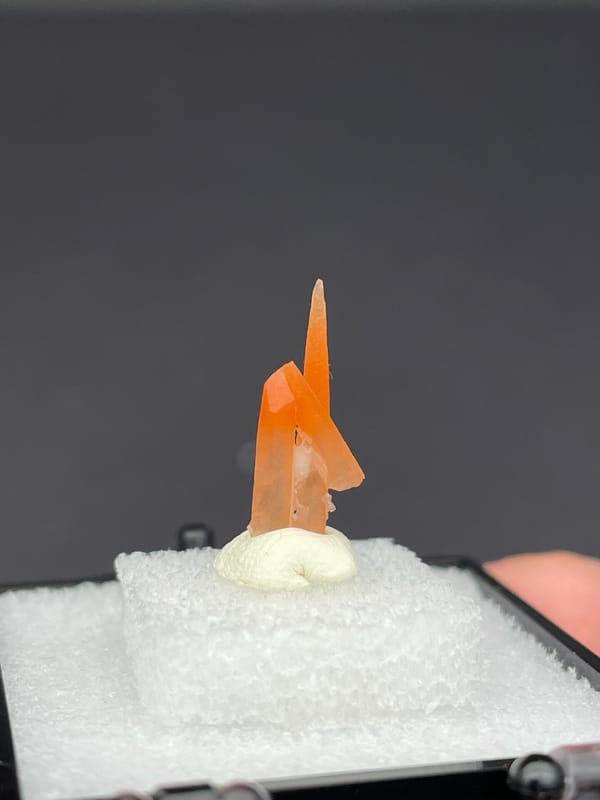 Slim orange-red hematoid quartz point from Guangdong, China, in a display box, reverse side