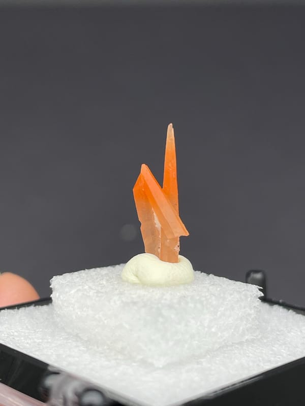 Slim orange-red hematoid quartz point from Guangdong, China, in a display box, detail of the matrix contact