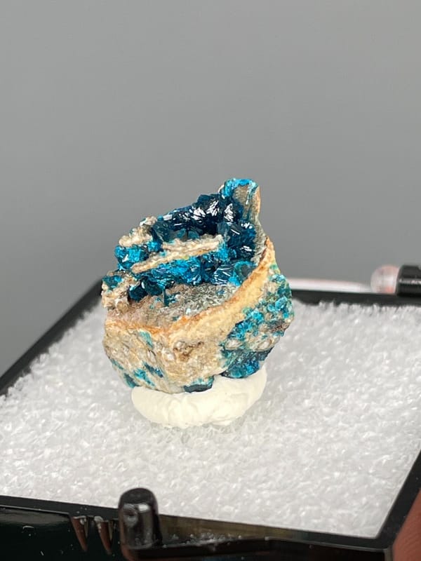 Blue veszelyite divided by a tan rock seam from Yunnan, China, in a box, close-up of the crystal faces
