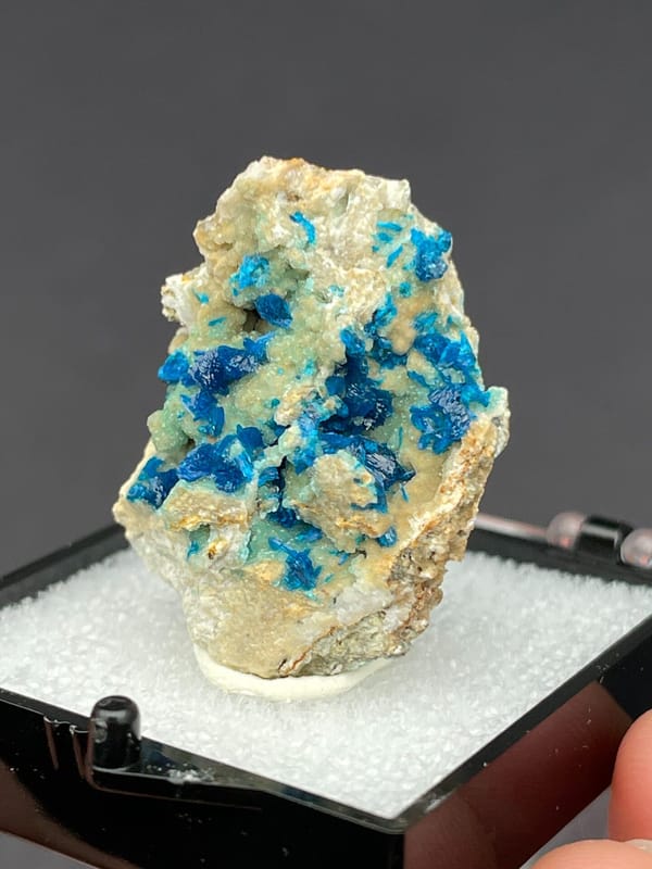 Blue veszelyite clusters scattered on a pale green matrix from Yunnan, China, close-up of the crystal faces