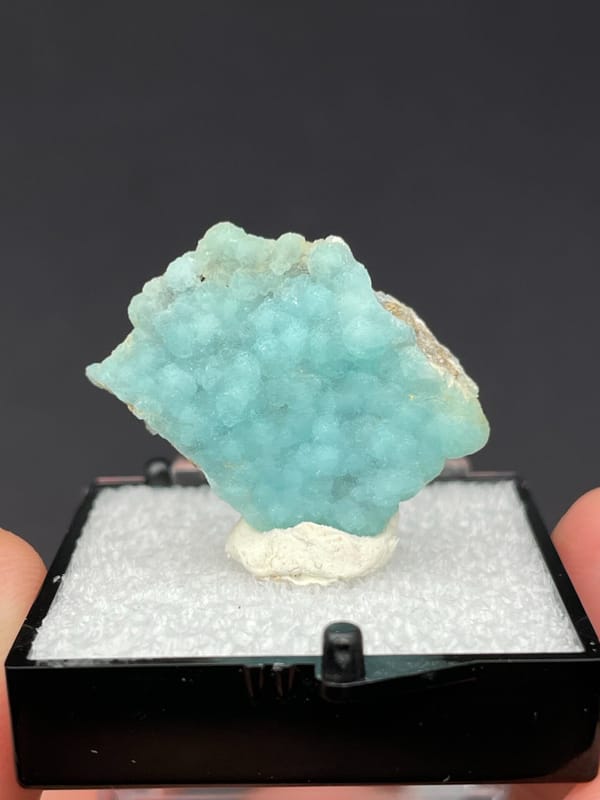 Pale turquoise botryoidal hemimorphite crust from Yunnan, China, in a display box, detail of the matrix contact