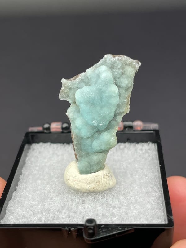 Pale blue-green botryoidal hemimorphite crust from Yunnan, China, in a display box, detail of the matrix contact
