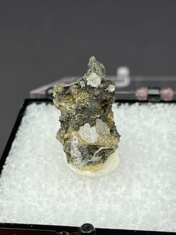 Colourless hemimorphite flower rosette on dark matrix from Guangxi, China, close-up of the crystal faces