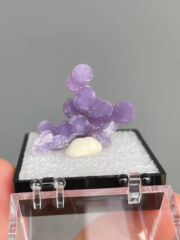 Cluster of purple botryoidal grape agate spheres from Indonesia, in a box, detail of the matrix contact
